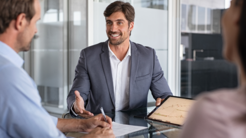 Financial advisor sharing account statements and fee disclosure documents across a wooden table with a couple during a retirement planning meeting.